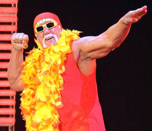 Hulk Hogan 穿著紅色服裝和黃色羽毛圍巾，在舞台上充滿活力地擺姿勢。 — 漫威標誌 壁紙