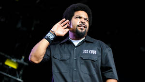 Ice Cube 在舞台上表演，手放在耳邊，身穿印有他名字的黑色襯衫。 — 冰塊 壁紙