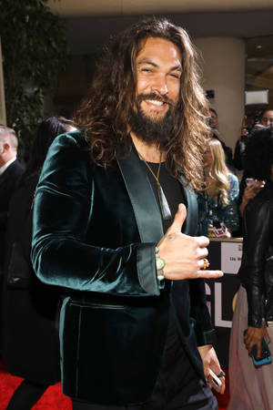 演員 Jason Momoa 在紅地毯上穿著藍綠色天鵝絨西裝外套，豎起大拇指。 — 傑森·摩莫亞 壁紙