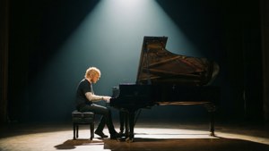 一位音樂家在黑暗舞台上於聚光燈下彈奏三角鋼琴。