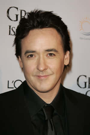 John Cusack 穿著黑色西裝和領帶在正式活動中。 — Oppo Pad 壁紙