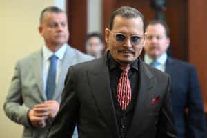 Johnny Depp 身穿深色西裝和紅色領帶，戴著太陽眼鏡在室內行走。 — 搞笑迷因 壁紙