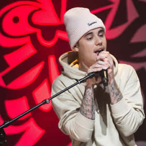 Justin Bieber 在舞台上對著麥克風唱歌，身穿米色連帽衫和白色無邊帽。 — 小賈斯汀 壁紙