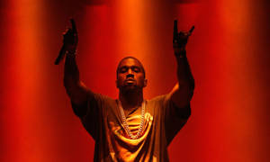 Kanye West 在紅燈下舉起雙臂在舞台上表演。 — 肯伊·威斯特 壁紙