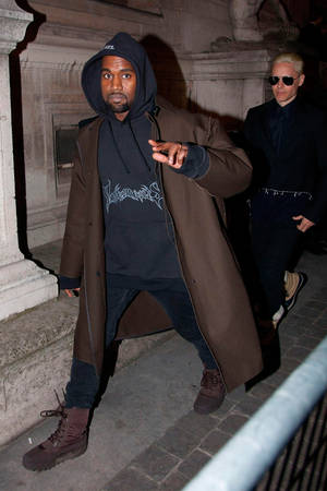 Kanye West 在夜間穿著外套和連帽衫走在石街上。 — 肯伊·威斯特 壁紙