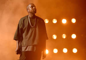 Kanye West 在溫暖的橙色燈光下在舞台上表演，身後有聚光燈。 — 肯伊·威斯特 壁紙