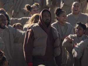 Kanye West 身穿栗色連帽衫，站在一群穿著米色長袍的歡呼人群中。 — 肯伊·威斯特 壁紙