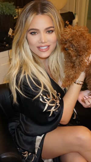 Khloé Kardashian 在室內穿著黑色絲質長袍，抱著一隻毛茸茸的棕色狗。