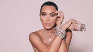 Kim Kardashian 手持香水瓶，佩戴閃亮珠寶，背景為粉紅色。 — 金·卡戴珊 壁紙