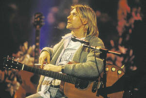 Kurt Cobain 在演唱會期間在舞台上彈奏木吉他，身後有觀眾。 — 肯伊·威斯特 壁紙