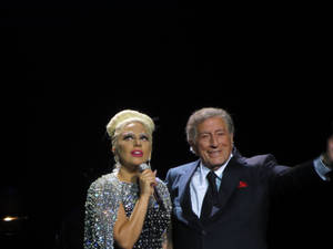 Lady Gaga 和 Tony Bennett 在表演期間於舞台上微笑。 — 暗色 壁紙