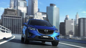藍色Mazda SUV在城市高速公路上行駛，後面有摩天大樓。 — 馬自達 壁紙