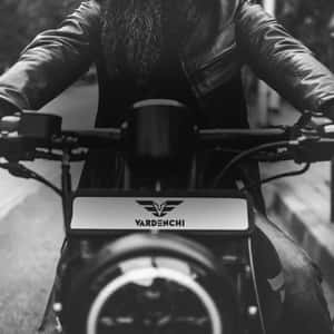 留鬍子的摩托車騎士在街上騎著VARDENCHI摩托車。 — 低飽和 壁紙