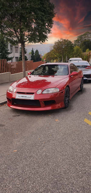 紅色Lexus跑車在充滿活力的夕陽下停泊在街上。 — iPhone 17e 壁紙