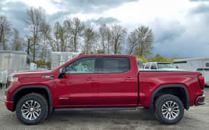 紅色雪佛蘭Silverado AT4皮卡車停放在碎石地上，附近有拖車和光禿禿的樹木。 — MacBook Pro M1 壁紙