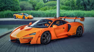 兩輛橙色McLaren超級跑車停在水邊，背景有綠色樹木。 — 酷炫F1 壁紙