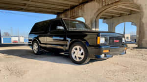 黑色GMC Typhoon SUV在陽光下停泊在混凝土天橋下。 — 1600x900 壁紙