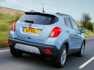 淺藍色Vauxhall Mokka SUV在鄉村道路上行駛，旁邊有綠色山丘。 — 歐寶 壁紙