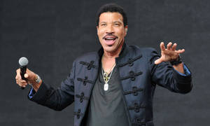 Lionel Richie 在舞台上用麥克風唱歌，表情豐富。 — 音樂 壁紙
