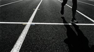 跑者越過跑道終點線，拖出長長影子