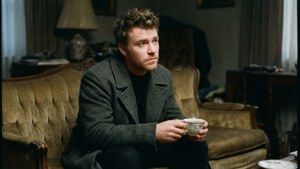 身穿灰色外套的男子在復古沙發上拿着茶杯。