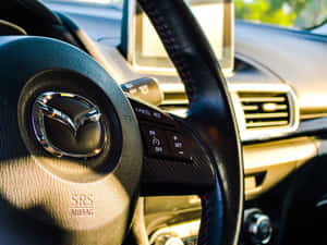Mazda 方向盤特寫，紅色縫線及鍍鉻徽章。