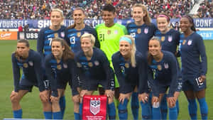 美國女子足球隊在草地上擺姿勢，身後有體育場觀眾。 — FIFA 世界盃 壁紙
