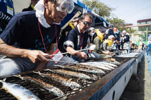 男士們在陽光明媚的戶外節日烤魚，有觀眾觀看。 — 白天 壁紙