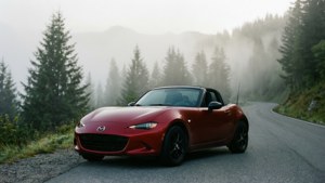 一輛紅色Mazda MX-5 Miata在清晨的山間薄霧道路上靜靜停放。