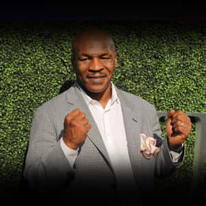 Mike Tyson 身穿千鳥格西裝外套，舉起拳頭在綠色樹籬前擺姿勢。 — 麥克·泰森 壁紙