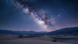 滿天繁星的夜空，銀河系橫跨沙漠沙丘和遠山。