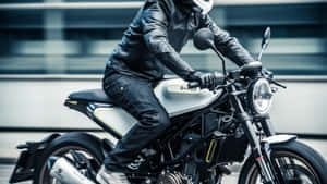 身穿皮衣的機車騎士，在城市街道上騎著一輛銀黑色機車。 — 改裝摩托車 壁紙