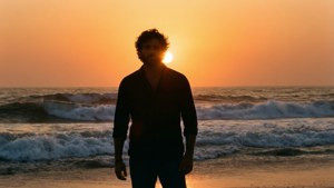 日落時分，男人剪影站在沙灘上，伴隨著海浪