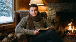 男人在雪中小屋的壁爐旁看書