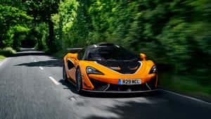 橙色McLaren在樹蔭大道上飛馳，帶動態模糊。 — 酷炫F1 壁紙