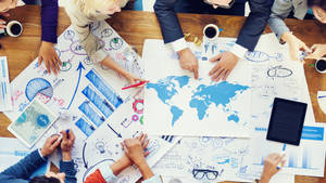 Business team brainstorming global strategy with maps and charts on a wooden table. — 工作 壁紙