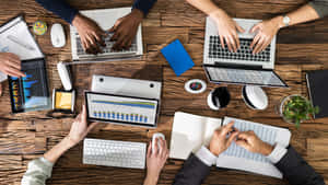 Team of professionals working together on digital devices at a wooden desk. — 筆電 壁紙