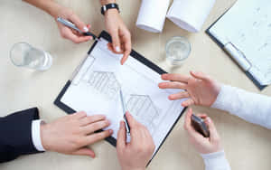 Four people reviewing architectural blueprints at a desk during a business meeting. — 房屋 壁紙