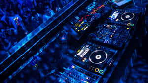 DJ booth with glowing controls and a crowd in a nightclub under blue lights. — 美學音樂 壁紙