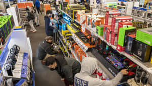 Shoppers browse gaming gear and electronics in a busy retail store aisle. — 最佳購買 壁紙