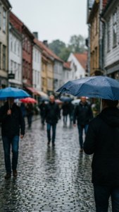 撐傘的行人在歷史建築之間的雨中鵝卵石街道上行走。