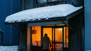冬天，一個人在被雪覆蓋的簷篷下進入溫暖明亮的建築物。