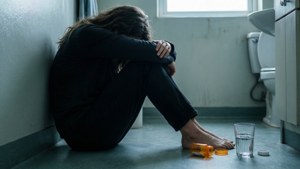 一個人獨自坐在浴室地板上，旁邊有一個藥瓶和一杯水。