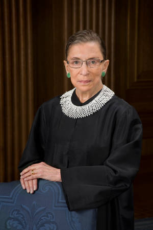 Ruth Bader Ginsburg 身穿法官袍，搭配蕾絲領和綠色耳環。 — 露絲·拜德·金斯伯格 壁紙