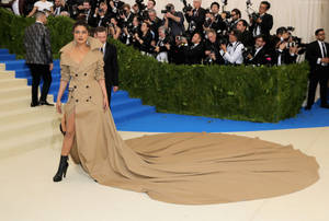 Priyanka Chopra 在一個晚會上穿著米色風衣長裙站在藍色地毯上。 — 琵豔卡·喬普拉 壁紙