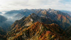 多雲天空下，色彩繽紛的森林和霧氣瀰漫的山谷的秋季山脈。