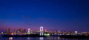 Rainbow Bridge 在黃昏時於東京灣上發光，城市燈光倒映在水中。 — 塔橋 壁紙