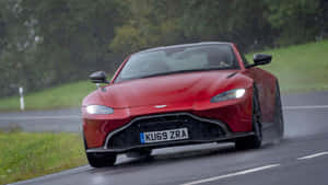 紅色Aston Martin在雨中於綠色鄉村的濕滑道路上飛馳。 — 奧斯頓馬丁 壁紙