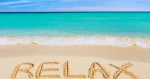 在熱帶沙灘的沙上寫著「relax」，有碧藍色海水和晴朗天空。 — 海灘 壁紙
