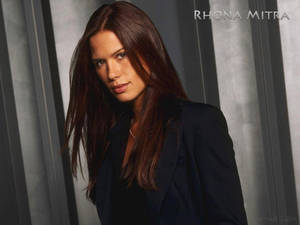 Rhona Mitra 身穿深色西裝外套，背景為灰色垂直條紋。 — 女演員 壁紙